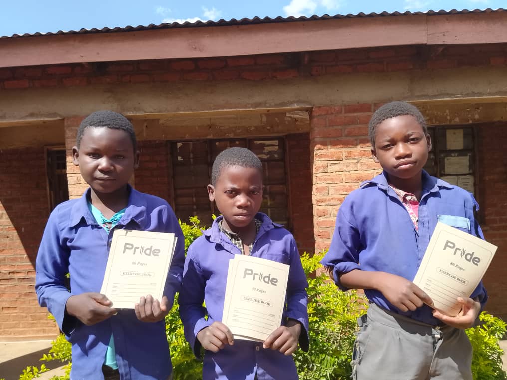Three boys in school uniforms holding Pride exercise books