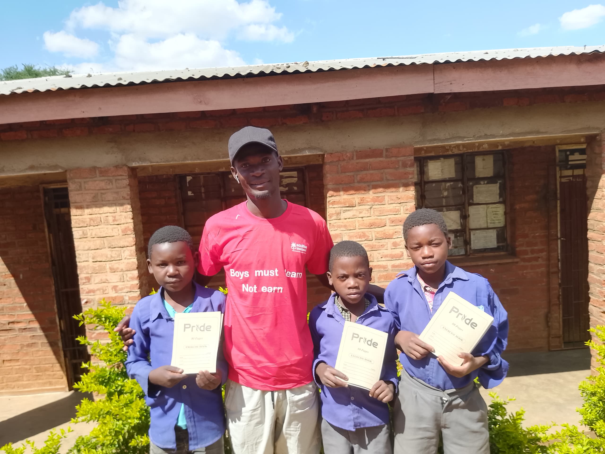 EduRise team member with three boys holding exercise books