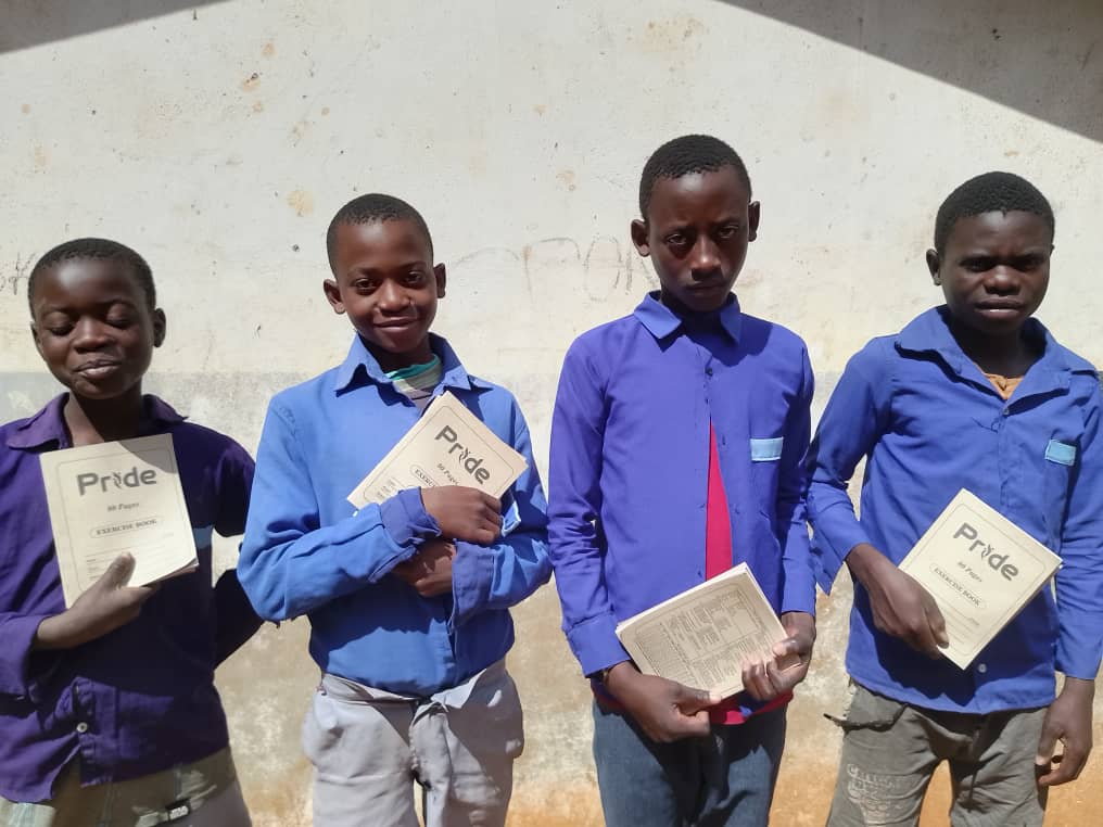 Four boys proudly showing their exercise books